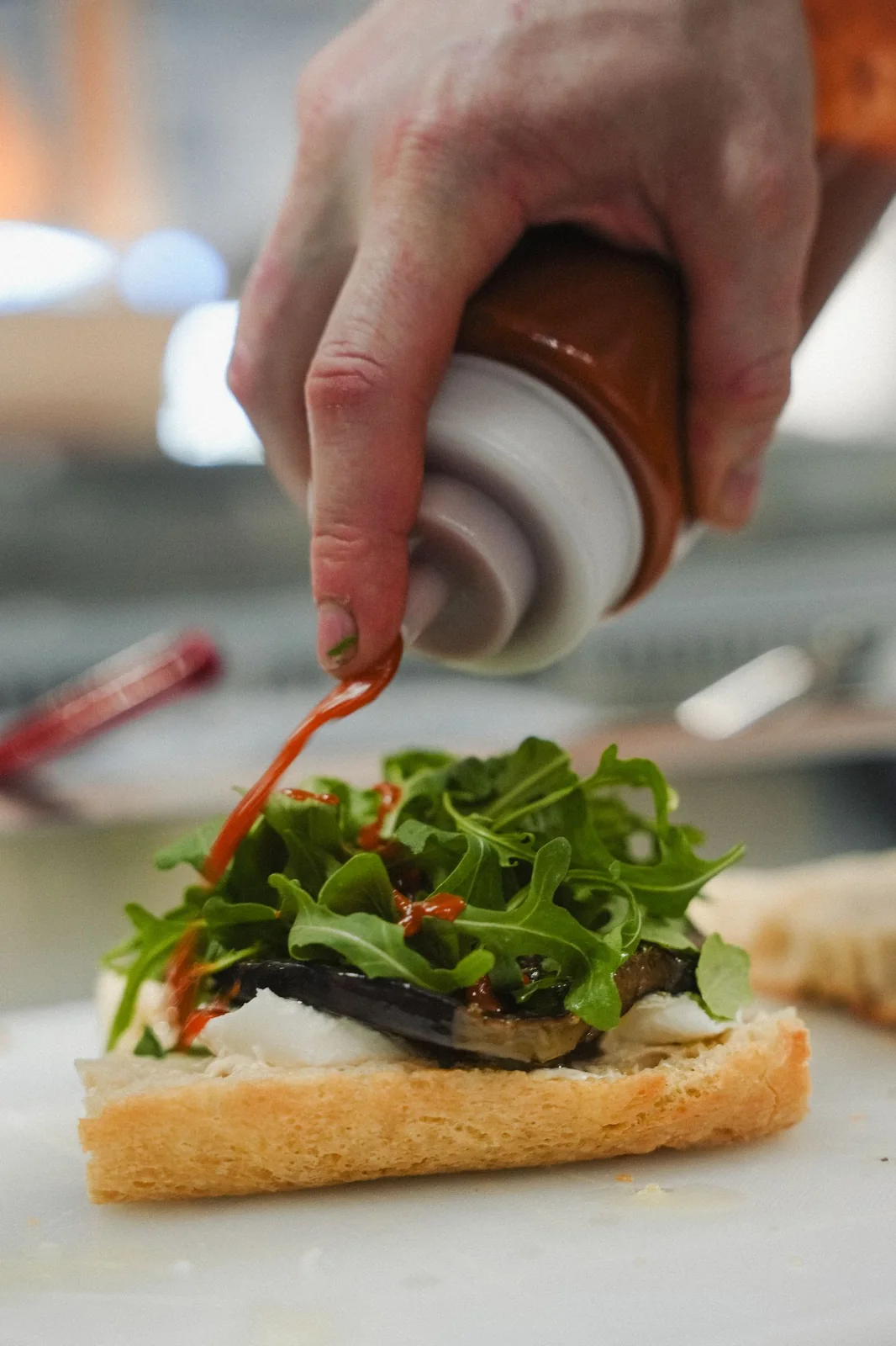 A hand finishing a grilled eggplant focaccia with sauce in the Mamma G's kitchen