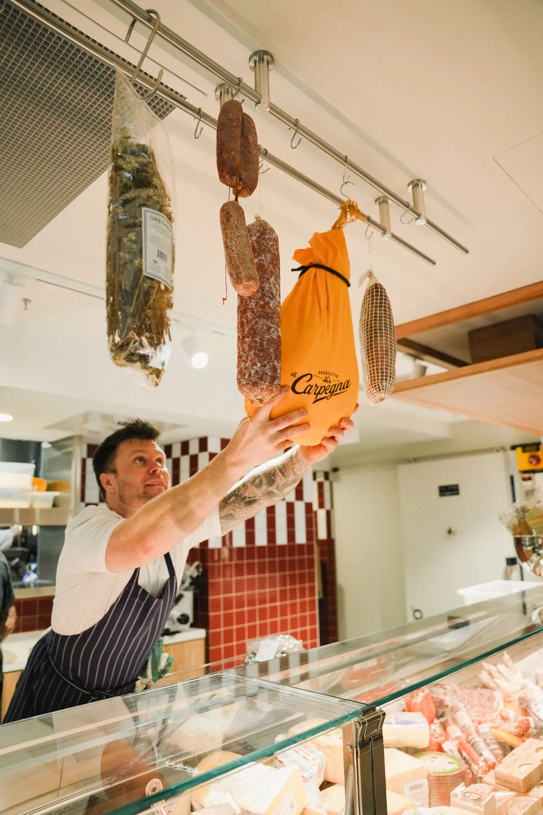 A chef reaching up to hang cured salumi above the deli counter