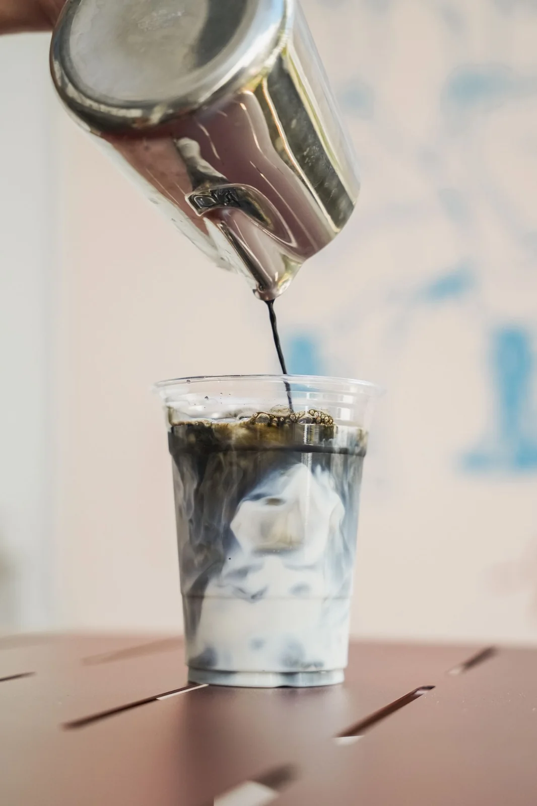 Espresso being poured over ice in a tall glass, in front of the blue nonna mural