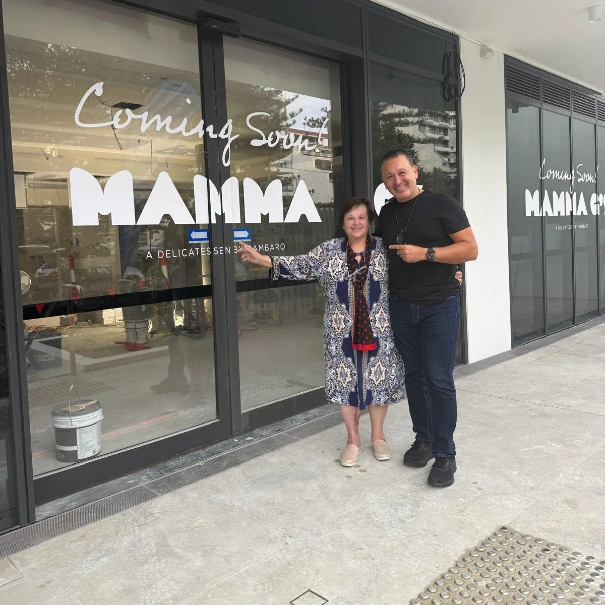 John Gambaro outside the Coolangatta shopfront with his mother Joyce, the Mamma G's of the name, the two of them pointing at each other beneath the window signage