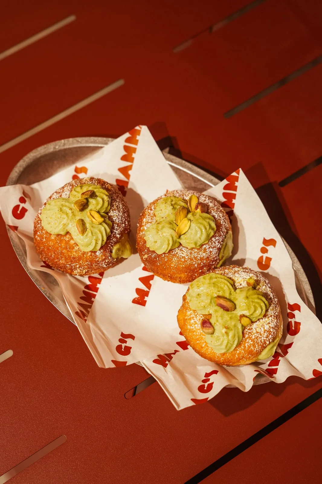 Three pistachio cream buns in a paper tray on Mamma G's branded wrapping paper