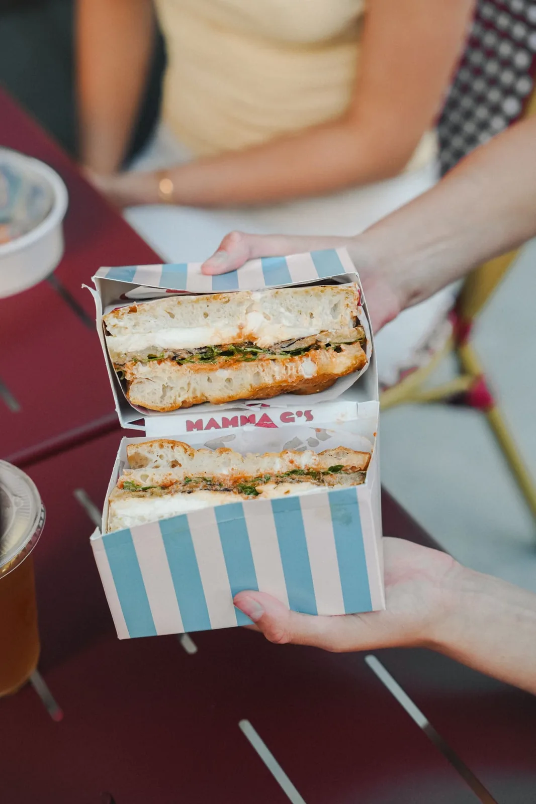 Striped Mamma G's boxes holding focaccia sandwiches on a red outdoor table
