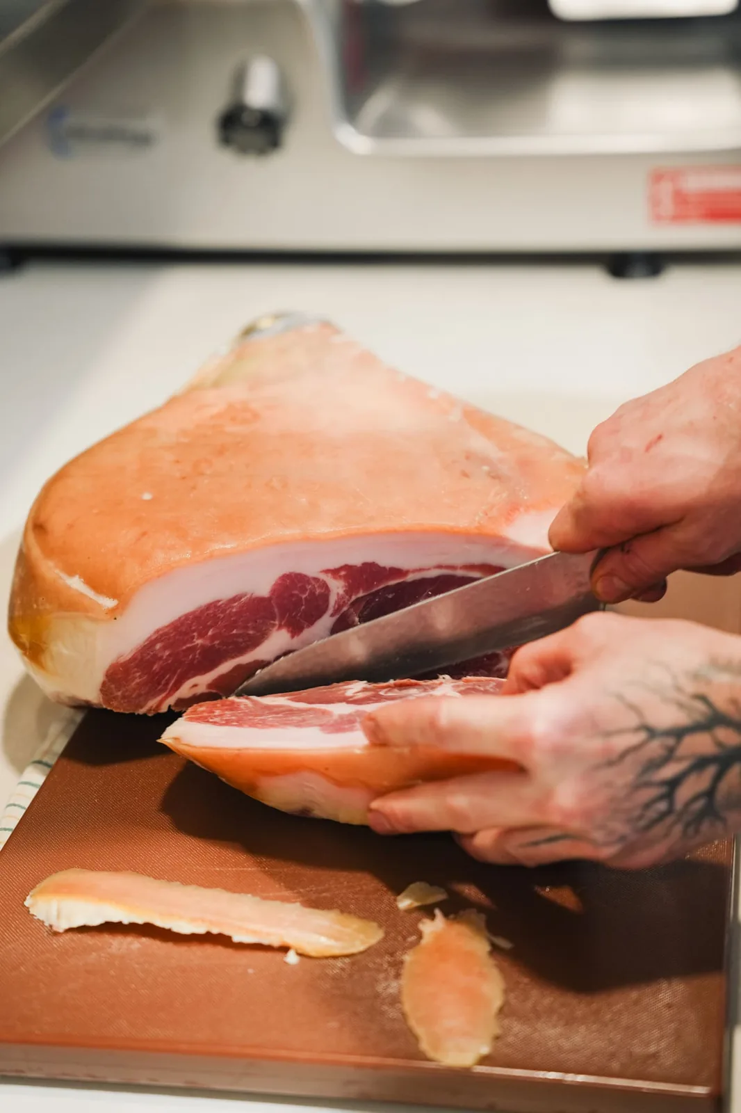 A hand slicing prosciutto by hand at the Mamma G's deli counter