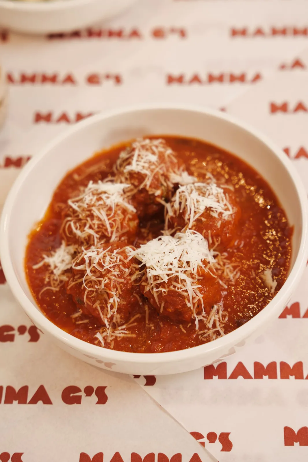 A bowl of meatballs in sugo topped with grated parmesan